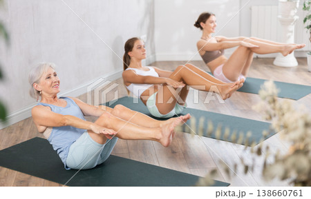 Three generation of women perform sitting lightweight variation of boat pose Paripurna Navasana 138660761