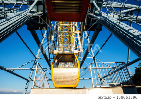 Symmetrical low angle shot of a yellow amusement park gondola against blue sky 138661396