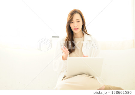 ノートパソコンを膝上に置いてオンラインの会話中の女性 ノートパソコンを膝上に置いてオンラインの会話中の女性 138661580