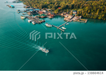 Aerial view of a traditional fishing village with a moving boat and clear emerald water. Aerial view of a traditional fishing village with a moving boat and clear emerald water. 138664614