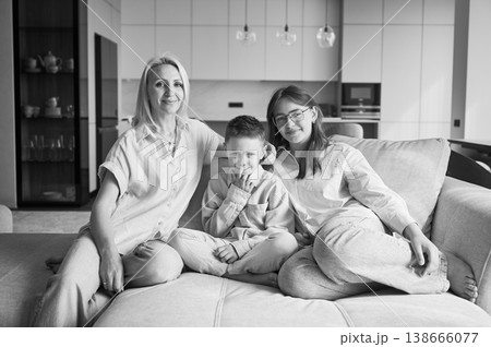 Cozy afternoon in family circle. Joyful children relaxing on couch with their mom. Cute moments of childhood. Cozy spending time with family indoors. Monochrome image. 138666077