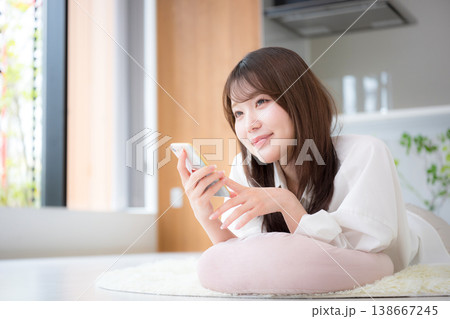 自宅でうつ伏せで寝転がるくつろぎながらスマートフォンを見る女性のリラックス 自宅でうつ伏せで寝転がるくつろぎながらスマートフォンを見る女性のリラックス 138667245