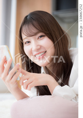 うつ伏せで寝転がるくつろぎながらスマートフォンを見る女性　クローズアップ 138667252