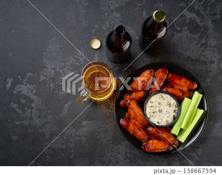 Spicy Buffalo wings with beer with and celery sticks on a dark table, top view. 138667594