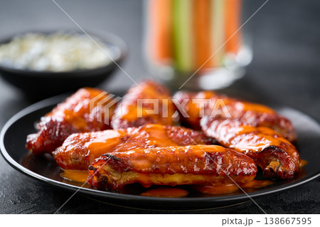 bbq buffalo chicken wings in a plate, with ranch dip, carrot and celery sticks on a dark table. bbq buffalo chicken wings in a plate, with ranch dip, carrot and celery sticks on a dark table. 138667595