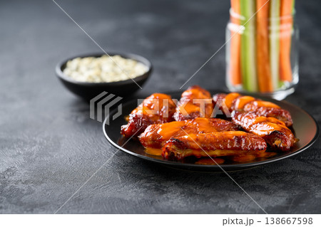 buffalo chicken wings. Fried bbq wings with celery and carrot vegetables and blue cheese sauce on a dark table. buffalo chicken wings. Fried bbq wings with celery and carrot vegetables and blue cheese sauce on a dark table. 138667598
