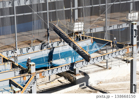 鉄骨建設現場で吊り荷をロープで誘導する作業員とクレーン揚重作業の様子11 138668150