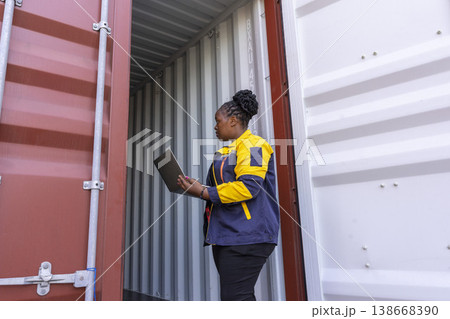 Black foreman woman worker talk on walkie-talkie at container yard, holding laptop computer. Logistics import export shipping concept. Black foreman woman worker talk on walkie-talkie at container yard, holding laptop computer. Logistics import export shipping concept. 138668390