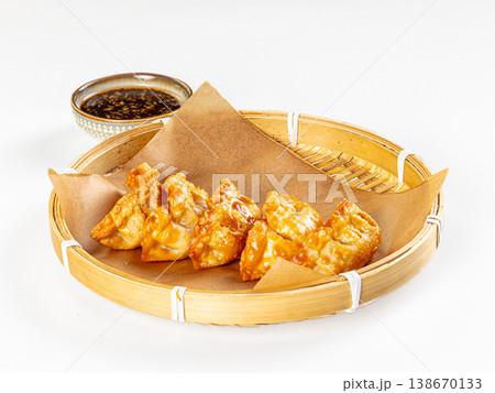 Crispy fried Asian dumplings in a bamboo basket with dipping sauce on a white background. Crispy fried Asian dumplings in a bamboo basket with dipping sauce on a white background. 138670133