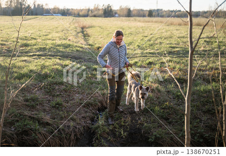 Woman walking dog on leash during countryside hike in green spring meadow Woman walking dog on leash during countryside hike in green spring meadow 138670251