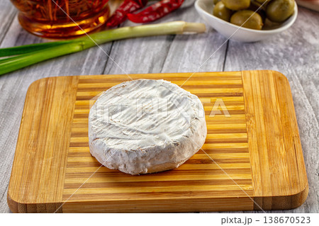 Round Camembert cheese on a wooden board with fresh vegetables and olives Round Camembert cheese on a wooden board with fresh vegetables and olives 138670523