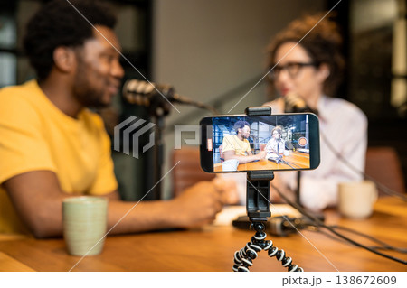 Diverse partners recording video podcast and looking at smartphone Diverse partners recording video podcast and looking at smartphone 138672609