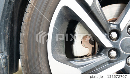 Front view of a metallic colored car wheel showing the brake disc and caliper inside. A dust covered mudguard is revealed indicating use in muddy environments. Front view of a metallic colored car wheel showing the brake disc and caliper inside. A dust covered mudguard is revealed indicating use in muddy environments. 138672707