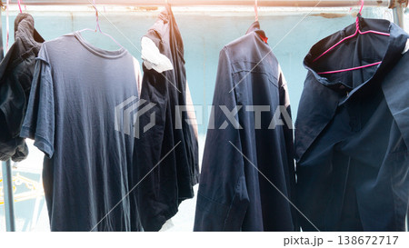 Dark colored shirt and trousers or blue in color. Are hanging on a clothesline outdoors. The background is a light blue house wall illuminated by artificial light. 138672717