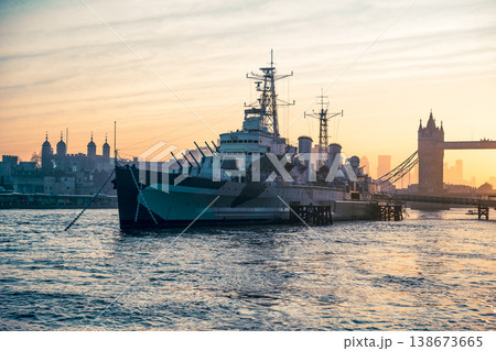 HMS Belfast is anchored in the River Thames in London. The morning light casts a warm glow on the ship and the nearby Tower Bridge. The scene shows an active city coming to life. HMS Belfast is anchored in the River Thames in London. The morning light casts a warm glow on the ship and the nearby Tower Bridge. The scene shows an active city coming to life. 138673665