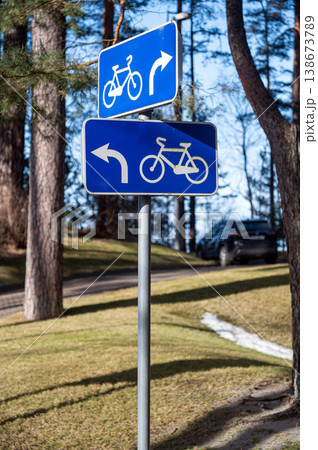 Signs show directions for cyclists in a park with trees and a car parked nearby. Signs show directions for cyclists in a park with trees and a car parked nearby. 138673789