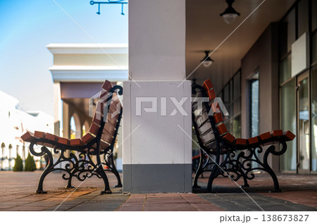 Benches sit side by side under a column in a shopping area during daylight hours 138673827