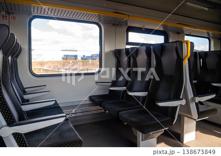 Several empty train seats are aligned in a clean train interior near a window during daytime. 138673849