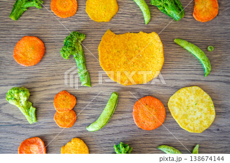 Seamless pattern of vegetable chips with broccoli carrot peas and sweet potato on wooden background. Healthy snack texture and clean eating concept. 138674144