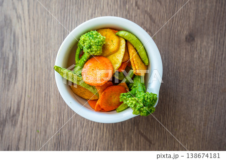 Mixed vegetable chips in bowl with broccoli, carrot, peas and sweet potato on wooden table. Healthy snack and clean eating concept without salt sugar or additives. Mixed vegetable chips in bowl with broccoli, carrot, peas and sweet potato on wooden table. Healthy snack and clean eating concept without salt sugar or additives. 138674181