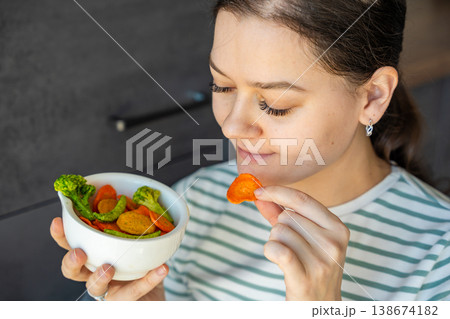 Woman eating vegetable chips from bowl as healthy snack at home. Clean eating and mindful diet concept with natural plant based food. Woman eating vegetable chips from bowl as healthy snack at home. Clean eating and mindful diet concept with natural plant based food. 138674182