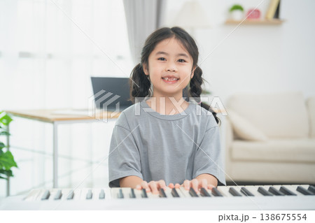 Joyful girl playing piano at home, wearing casual gray t-shirt, smiling in bright living room with modern decor and natural light 138675554