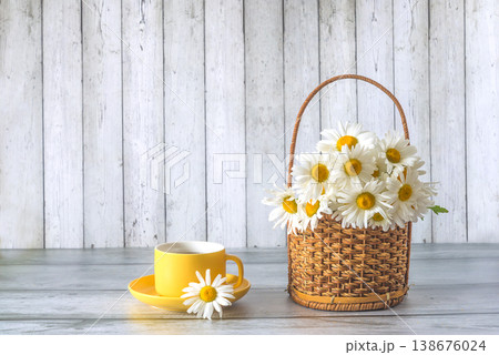 Bouquet of white daisies or chamomile flowers in wicker basket and yellow cup of tea on a wooden background; copy space Bouquet of white daisies or chamomile flowers in wicker basket and yellow cup of tea on a wooden background; copy space 138676024