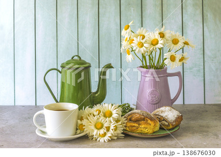 Summer breakfast still life; cup of coffee, hot croissants, bouquet of white daisies and vintage coffee pot on a table 138676030