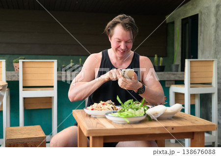 Smiling Caucasian Man Using Smartphone While Dining on Thai Isan Food at Outdoor Restaurant Smiling Caucasian Man Using Smartphone While Dining on Thai Isan Food at Outdoor Restaurant 138676088