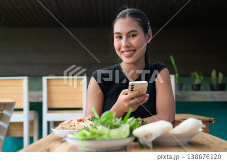 Smiling Young Thai Woman Using Smartphone at Restaurant Table with Traditional Isan Food Copy Space Smiling Young Thai Woman Using Smartphone at Restaurant Table with Traditional Isan Food Copy Space 138676120