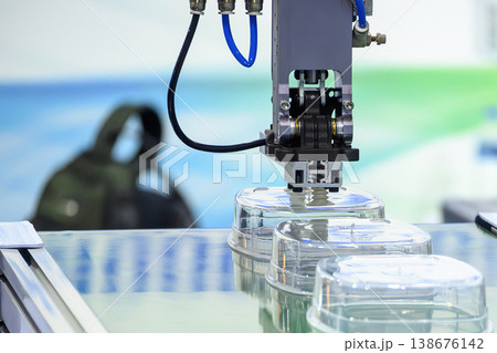Industrial robotic arm placing plastic food containers onto a conveyor belt from an injection molding machine. Industrial robotic arm placing plastic food containers onto a conveyor belt from an injection molding machine. 138676142