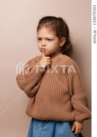 Young child girl covering mouth signaling silence or secret on beige background 138676301