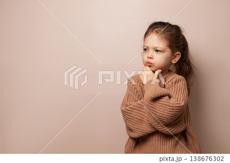 cute little child girl pouting and looking away with arms crossed, wearing a brown knit sweater, copy space 138676302
