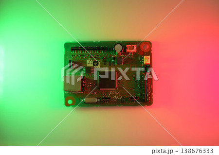 Colorfully lit circuit board (PCB) featuring a central microchip, connectors and electronic components on a red-to-green gradient background. Technology, innovation, electronics design. Colorfully lit circuit board (PCB) featuring a central microchip, connectors and electronic components on a red-to-green gradient background. Technology, innovation, electronics design. 138676333