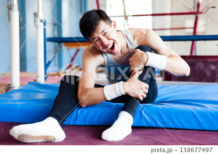 Injured male gymnast suffering from knee pain after bad landing Injured male gymnast suffering from knee pain after bad landing 138677497