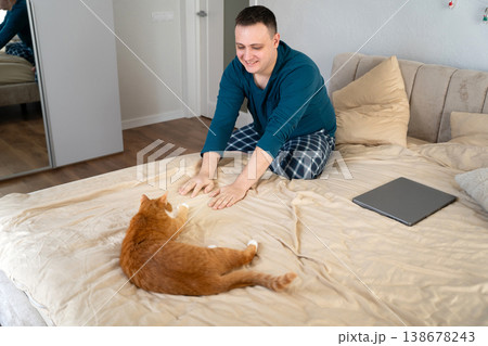 A young caucasian 35 old caucasian man play with their ginger cat on a bed A young caucasian 35 old caucasian man play with their ginger cat on a bed 138678243