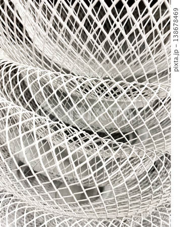 Layered arrangement of white wire mesh formed into curves and spirals. Light highlights gaps and lines in material, interesting patterns. Thin wires twisted together to form large, open shape 138678469