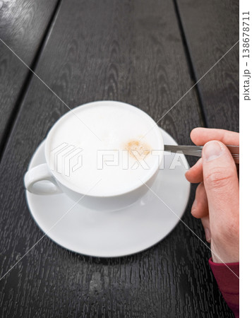 Creamy coffee cup Cappuccino with frothy milk and a spoon held by a hand on a dark wooden table concept. copy space Creamy coffee cup Cappuccino with frothy milk and a spoon held by a hand on a dark wooden table concept. copy space 138678711