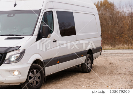 White commercial cargo van parked on a gravel road near autumn trees during daytime. White commercial cargo van parked on a gravel road near autumn trees during daytime. 138679209