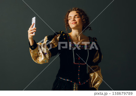 Portrait of a young aristocratic woman holding mobile phone dressed in a medieval dress on dark background Portrait of a young aristocratic woman holding mobile phone dressed in a medieval dress on dark background 138679789