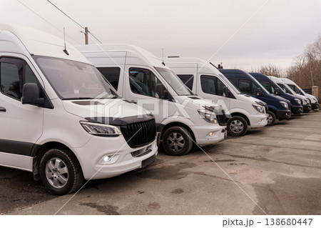 Row of white and dark delivery vans parked on asphalt lot under overcast sky in outdoor setting. 138680447