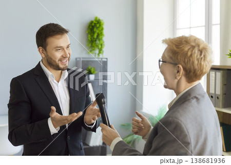 Reporter handing microphone to business speaker during interview in modern office Reporter handing microphone to business speaker during interview in modern office 138681936