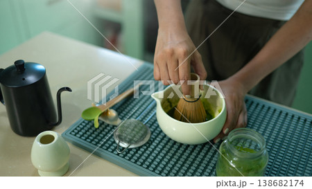 Hands whisking matcha powder in ceramic bowl on kitchen counter. Hands whisking matcha powder in ceramic bowl on kitchen counter. 138682174