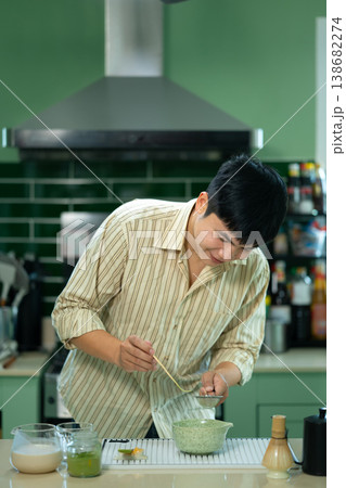 Man hands sifting matcha powder into a traditional bowl for green tea preparation at kitchen home Man hands sifting matcha powder into a traditional bowl for green tea preparation at kitchen home 138682274