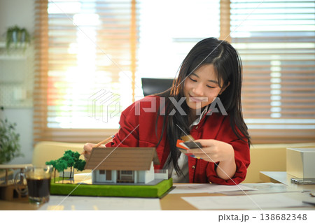 Architect woman selecting material samples beside house model, Professional architect reviewing materials for design project. Architect woman selecting material samples beside house model, Professional architect reviewing materials for design project. 138682348