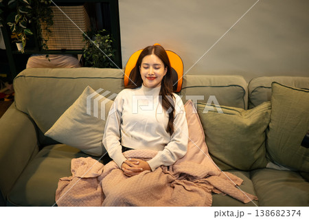 Relaxed woman using neck massager on sofa at home Relaxed woman using neck massager on sofa at home 138682374