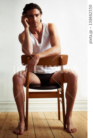 Sexy, portrait of young man on chair by white wall with underwear for strong, body building and hot muscles. Serious, attractive and handsome male model posing with confidence on wood stool with vest 138682550