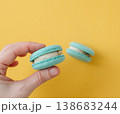 Woman hand holding turquoise macaron against yellow background, showing texture with high contrast colors 138683244