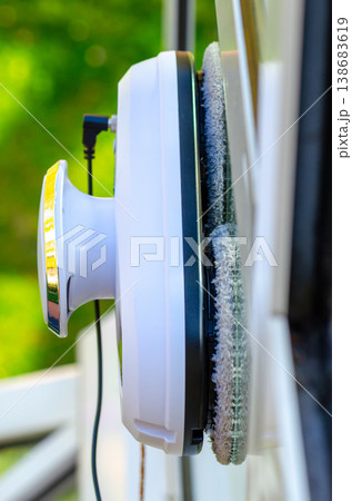 Window cleaning robot attached to glass cleans window surface with green nature background in bright light Window cleaning robot attached to glass cleans window surface with green nature background in bright light 138683619