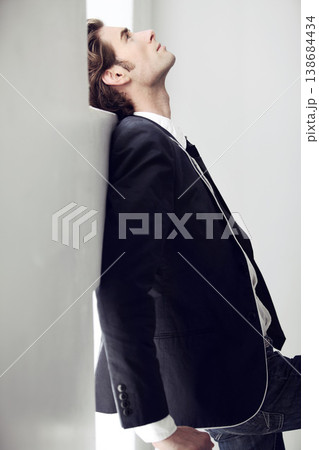 Depressed, sad and young man with fashion for formal style by a white wall in a modern home. Profile, classy style and male person from Canada in elegant suit with mental health issue in a space. 138684434